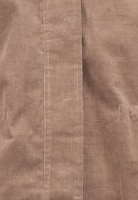 Tela de pana marrón con costuras verticales, con costuras contrastantes y una textura suave. Diseño sencillo sin hardware ni acentos visibles.