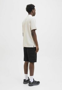 Beige polo shirt with short sleeves, black cargo shorts, white socks, and black athletic shoes, worn by a person from the back.