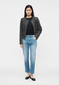 Svart jeansjacka med tryckknappar, bärs över en svart topp. Ljusblå jeans med raka ben och svarta balettskor fullbordar outfiten.