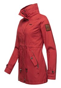 Red jacket with high collar, two front pockets, drawstring waist, and logo patch on sleeve. Made from a durable fabric with a smooth texture.