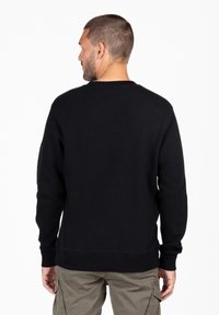 Felpa nera con maniche lunghe, texture a coste e scollatura girocollo, abbinata a pantaloni cargo kaki.