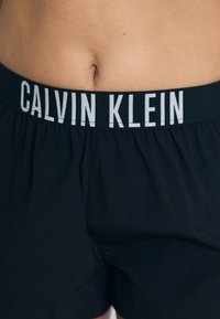 Boxers Calvin Klein noirs avec une ceinture contrastante vert foncé ornée d'un texte logo blanc. Fabriqués en tissu doux avec une coupe élastique.