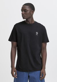 Tricou din bumbac negru cu mâneci scurte, gât rotund și un grafic brodat pe față. Purtați cu pantaloni scurți din denim albastri.