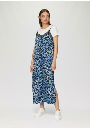 Robe maxi à imprimé léopard en bleu avec des accents en dentelle sur les bretelles. Fentes latérales notables, portée par-dessus un t-shirt blanc, assortie à des baskets blanches.