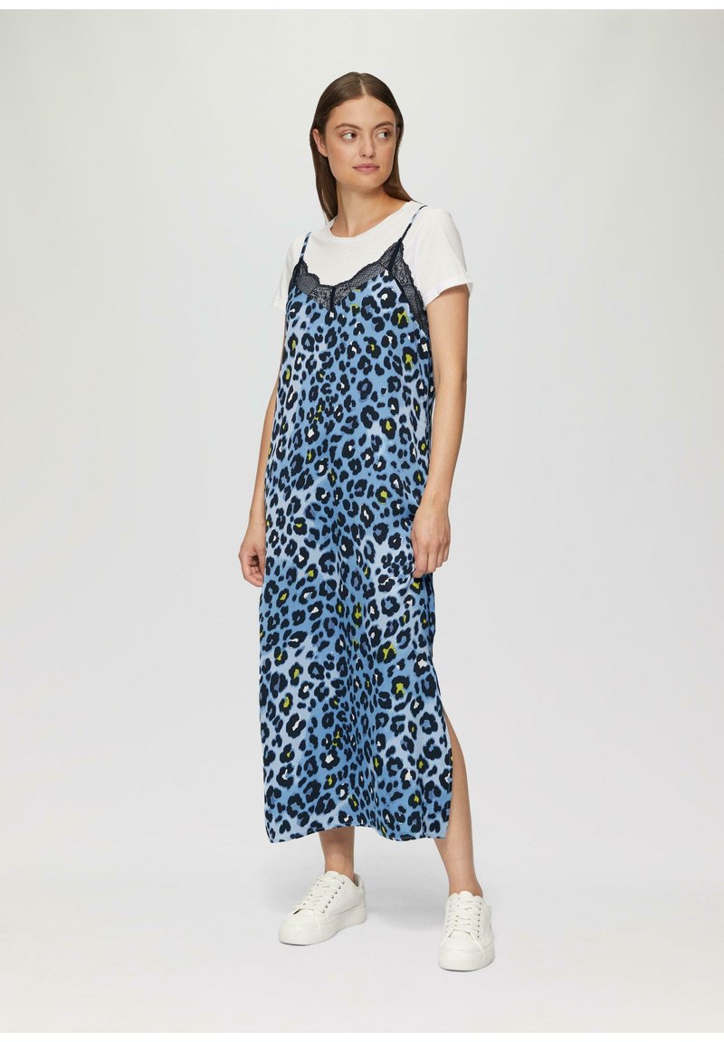 Maxi jurk met luipaardprint in het blauw, met kantaccenten op de schouderbandjes. Opvallende zijsplits, gedragen over een wit T-shirt, gecombineerd met witte sneakers.