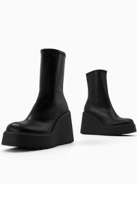 Black leather ankle boots featuring a wedge sole, smooth texture, rounded toe, and minimal stitching detail.
