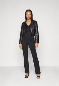 Black cropped leather jacket with a single button, paired with black fitted pants and strappy black high-heeled sandals. Smooth texture.