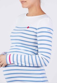 Langarm-Maternity-Shirt in Weiß mit blauen Streifen und einem roten Herzsymbol auf der Brust. Verfügt über ein tailliertes Design und weiche Materialien.