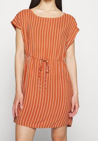 Rostfärgad klänning med vita vertikala ränder, rund halsringning, korta ärmar och knytning i midjan. Tillverkad av lättviktsmaterial.