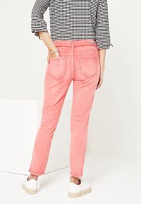 Jeans de mezclilla rosa con ajuste slim y cinco bolsillos, combinados con una blusa de cuadros en blanco y negro y zapatos de esparto blancos.