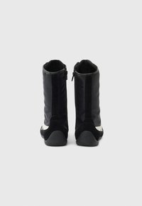 Černé kotníkové boty s hladkou texturou, vybavené zipem na zadní straně a kontrastním bílým prvkem na boku.