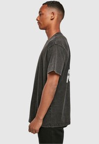 Zwarte katoen t-shirt met een losse pasvorm, korte mouwen en een ronde hals. Heeft een verouderde textuur en witte logo detail op de achterkant.