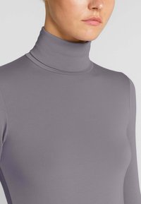 Maglia a maniche lunghe con colletto a polo in lavanda tenue, realizzata in un tessuto liscio ed elastico che segue la forma del corpo senza ulteriori dettagli o motivi.