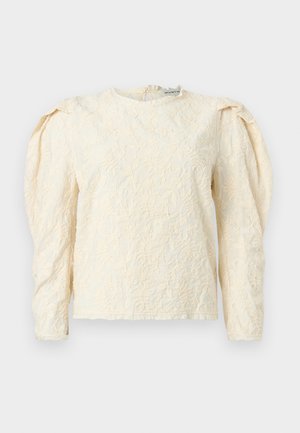 Κρέμ μακρυμάνικη μπλούζα με υφασμένο λουλουδάτο σχέδιο, σούρες στους ώμους και στρογγυλή λαιμόκοψη. Διακριτική λάμψη με απαλό φινίρισμα υφάσματος.