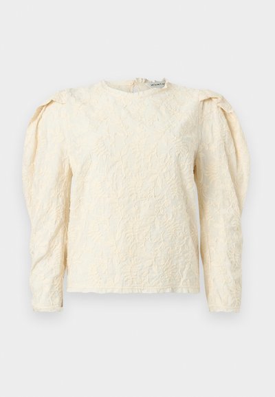 Κρέμ μακρυμάνικη μπλούζα με υφασμένο λουλουδάτο σχέδιο, σούρες στους ώμους και στρογγυλή λαιμόκοψη. Διακριτική λάμψη με απαλό φινίρισμα υφάσματος.