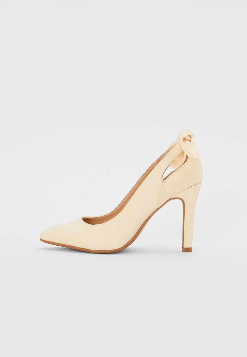 Scarpa col tacco alta beige con punta affilata, tomaia in similpelle liscia, design con ritagli e dettaglio di fiocco alla caviglia.