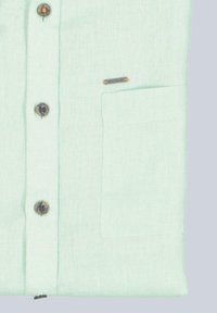 Hellgrüles Leinenhemd mit einer Brusttasche, ausgestattet mit runden Knöpfen mit dunklen Zentren und einem kleinen Markenschild mit orangefarbenen Akzenten.