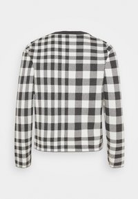 Veste à carreaux noir et blanc avec des manches longues, un col rond, et un tissu texturé présentant des motifs de carreaux variés sur la surface.