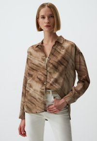 Bruine gestreepte shirt met een ontspannen pasvorm, met knopen dicht, kraagontwerp, gemaakt van lichte stof, gecombineerd met witte broek.