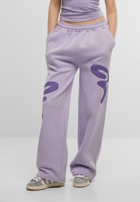 Lavendelfärgade sweatpants med elastisk midja, vida ben och mörklila abstrakta mönster på framsidan. Mjuk tygstruktur och avslappnad passform.