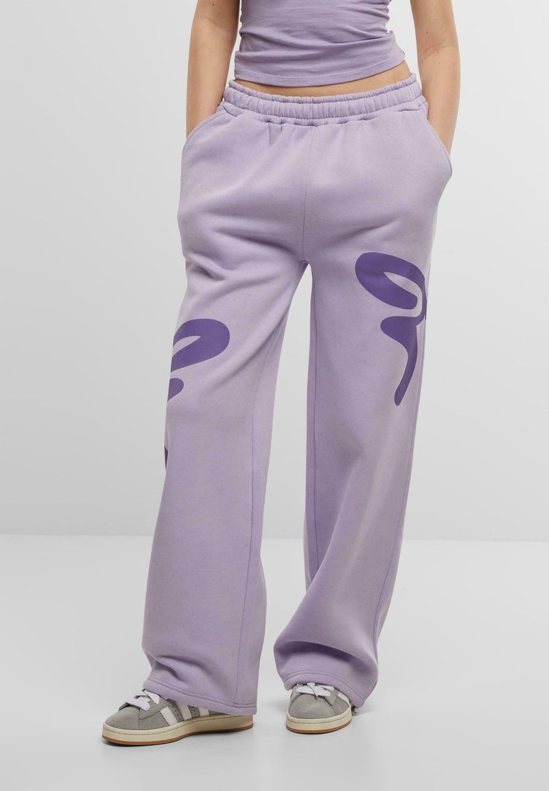 Lavendelfärgade sweatpants med elastisk midja, vida ben och mörklila abstrakta mönster på framsidan. Mjuk tygstruktur och avslappnad passform.