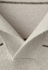 Tissu tricoté beige clair montrant un gros plan sur un col en V avec une texture tricotée visible et des détails de points fins.