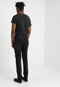 Camiseta de algodón negra con un corte relajado y mangas enrolladas, combinada con jeans negros slim-fit, vista desde la parte trasera con un fondo neutro.