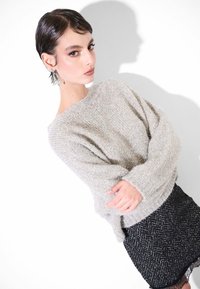 Maglione grigio chiaro con texture, vestibilità ampia e maniche lunghe, abbinato a una gonna nera a spina di pesce. Tessuto con una sottile brillantezza.