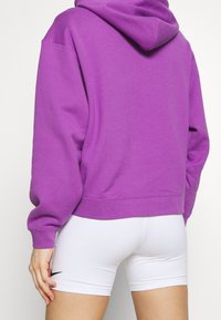 Felpa con cappuccio viola realizzata in tessuto misto cotone, con tasca a marsupio e polsi a coste, abbinata a pantaloni corti bianchi aderenti.