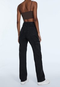 Pantalones cargo negros de cintura alta, con piernas anchas, bolsillos laterales y traseros, combinados con un top corto ajustado marrón. Textura suave.