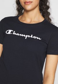 Námořnické modré bavlněné tričko s bílým kurzivním logem "Champion" přes hruď. Klasický kulatý výstřih a krátké rukávy.