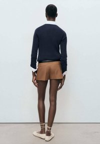 Marine trui met witte kraag, beige shorts en beige schoenen. Glad stof, getailleerd ontwerp, met opvallende enkelbandjes op de schoenen.