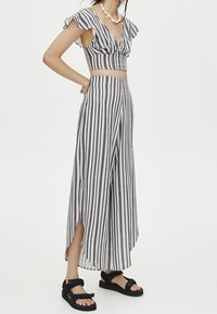 Gestreepte zwart-witte two-piece outfit met een cropped top met volants en wijde broek met zijsplitten; gecombineerd met zwarte sandalen.
