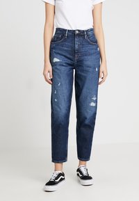 Blå denimjeans med lös passform, med slitna detaljer och hög midja. Matchas med svartvita sneakers.