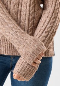Sweter z warkoczykiem w miękkim beżowym materiale, z prążkowanymi mankietami i teksturowanymi wzorami. Projekt obejmuje gruby splot i luźny krój.
