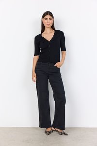 Mustaa neulottua neuletakkia, jossa on aaltoileva kaula-aukko, lyhyet hihat ja nappikiinnitys, yhdistettynä korkeavyötäröisiin mustiin leveälahkeisiin farkkuihin ja raidallisiin korkokenkiin.