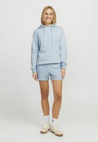 Sweatshirt bleu clair avec capuche et poche avant, associé à un short assorti. Le tissu est doux ; il est doté d'une coupe décontractée et de poignets côtelés.