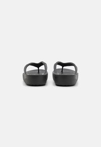 Sandales en caoutchouc noires avec une texture lisse, bout ouvert et un design de bride simple. Dotées d'une semelle intérieure à motifs et d'une semelle extérieure texturée.