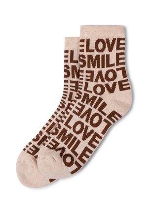 Beżowe skarpetki z powtarzającymi się brązowymi wzorami tekstu z napisami "LOVE" i "SMILE" w różnych orientacjach, wyłożone płasko na białym tle.
