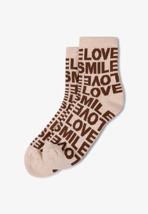 Beżowe skarpetki z powtarzającymi się brązowymi wzorami tekstu z napisami "LOVE" i "SMILE" w różnych orientacjach, wyłożone płasko na białym tle.