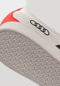 Weißer Sneaker mit korallenfarbenem Absatz, einer strukturierten Gummisohle, schwarzem Logodetail und glattem Obermaterial.