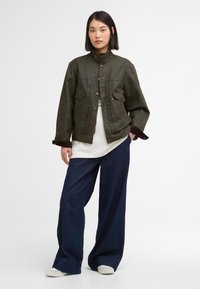 Σκούρο πράσινο, ανθεκτικό μπουφάν από ύφασμα με όρθιο γιακά, μπροστινές τσέπες και κουμπιά. Φοριέται πάνω από ένα λευ�κό πουκάμισο και συνδυάζεται με μπλε παντελόνια με φαρδιά καμπάνα.