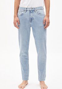 Jasnoniebieskie dżinsy z denimu o prostym kroju nogawki, z pięcioma kieszeniami i zapięciem na metalowy guzik. Materiał cechuje się miękką, lekko zużytą fakturą.