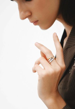 Anillos entrelazados de plata y oro llevados en un dedo, destacando un acabado suave y pulido sobre un fondo neutro.