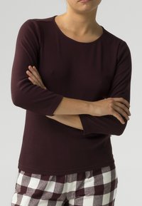 Burgundowy top z długim rękawem wykonany z prążkowanej tkaniny, z okrągłym dekoltem i dopasowanym krojem, w zestawieniu z czarno-białymi spodniami w kratę.