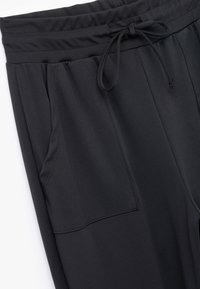 Black jogger pants made from smooth fabric, featuring an elastic waistband with a drawstring, side pockets, and stitched detailing.