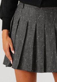 Plisséskirt in een zwart-wit visgraatpatroon, gemaakt van een textuurstof. Heeft een gedefinieerde tailleband en een subtiele glans.