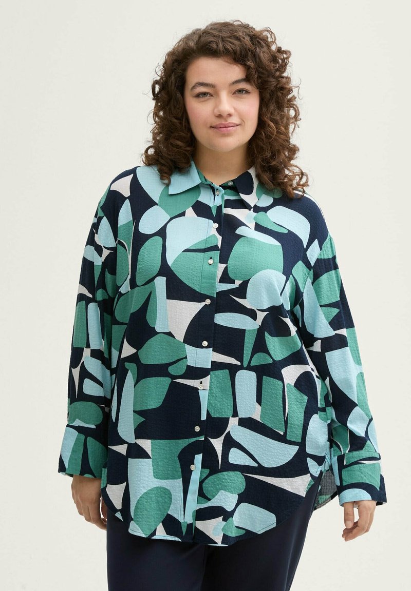 Chemise ornée d'un motif de formes irrégulières en bleu marine foncé, bleu clair et vert. Elle possède un col et une fermeture à boutons sur le devant.