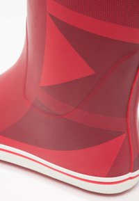 Botte en caoutchouc rouge avec une surface lisse ornée de motifs géométriques, une semelle blanche avec des accents rouges et un design à bout rond.
