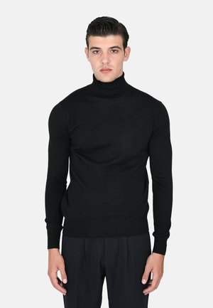 Maglione a collo alto nero realizzato in tessuto morbido, design aderente con maniche lunghe, polsini e orlo a costine, indossato con pantaloni neri.